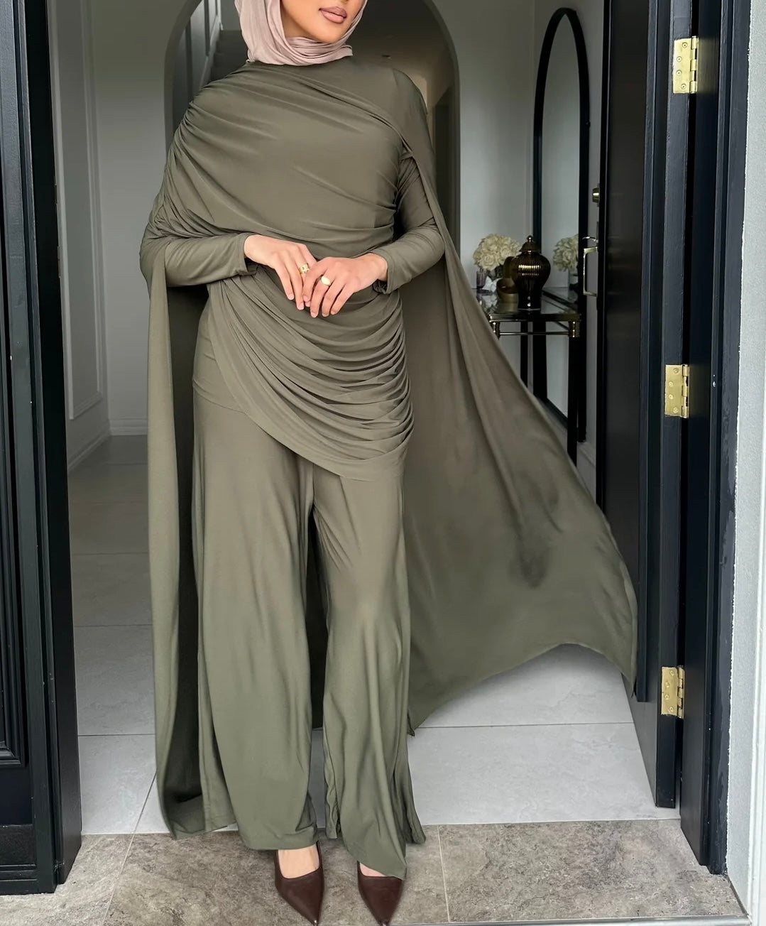Person wearing a long, flowing olive green outfit with a matching hijab in a room.