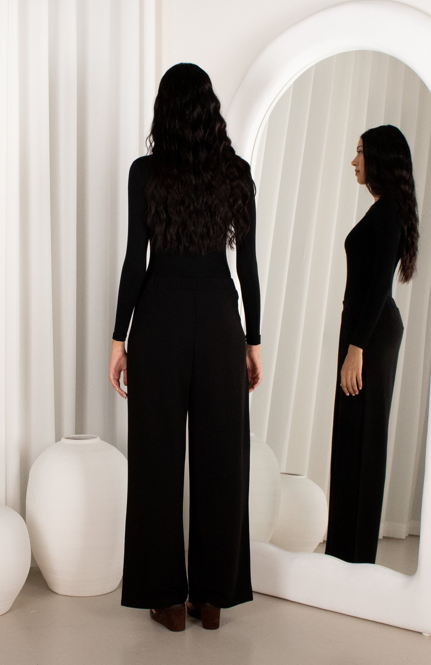 Woman wearing a black jumpsuit standing in front of a mirror.