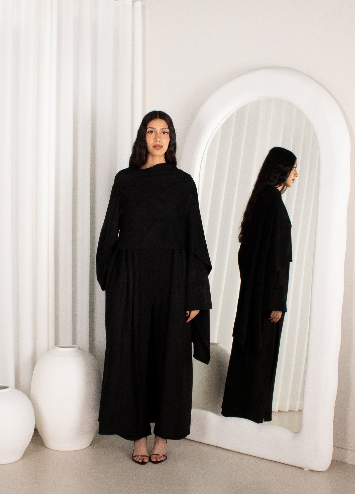Woman in a black outfit standing in front of a white mirror.