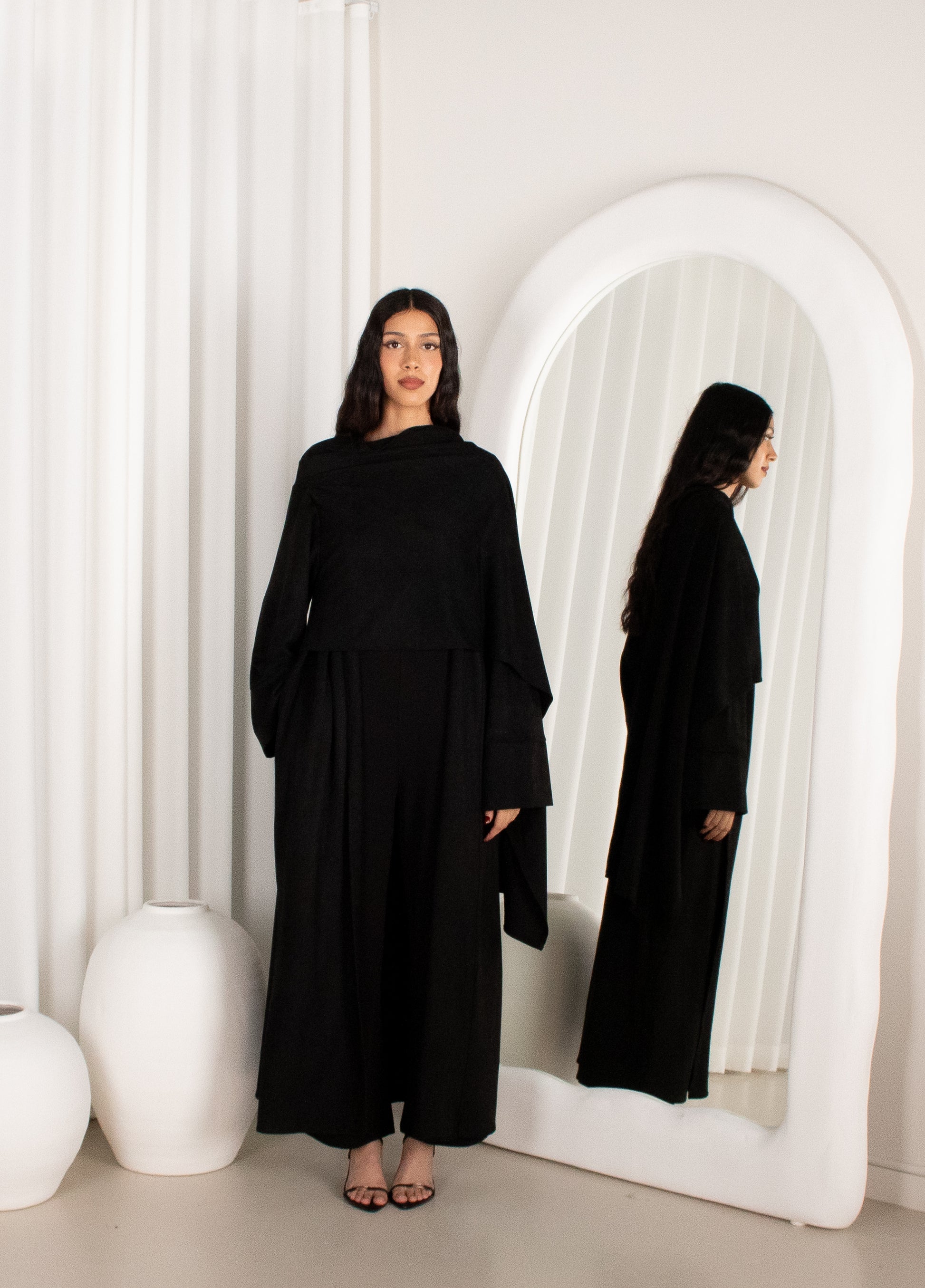 Woman in a black outfit standing in front of a white mirror.