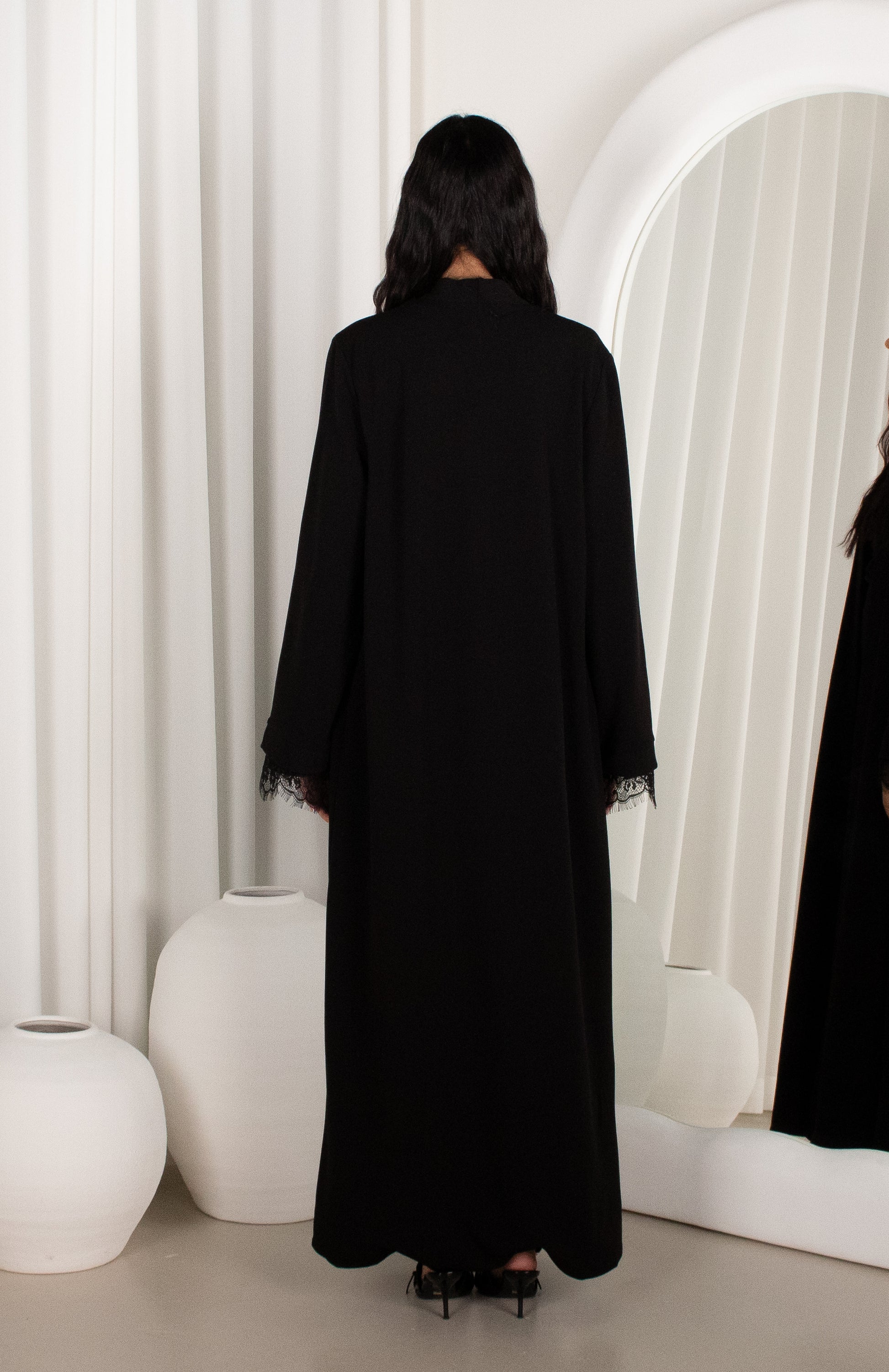 Person wearing a black abaya in a minimalistic room with white decor.