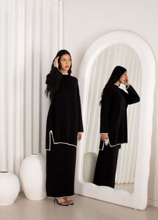 Woman in a black dress standing in front of a mirror in a minimalistic room.