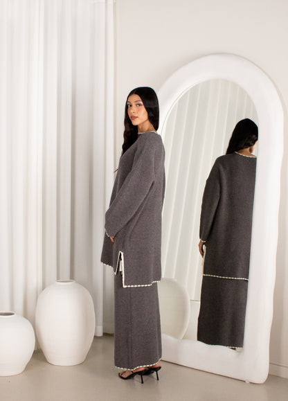 Woman in a gray dress standing in front of a white mirror in a minimalistic room.