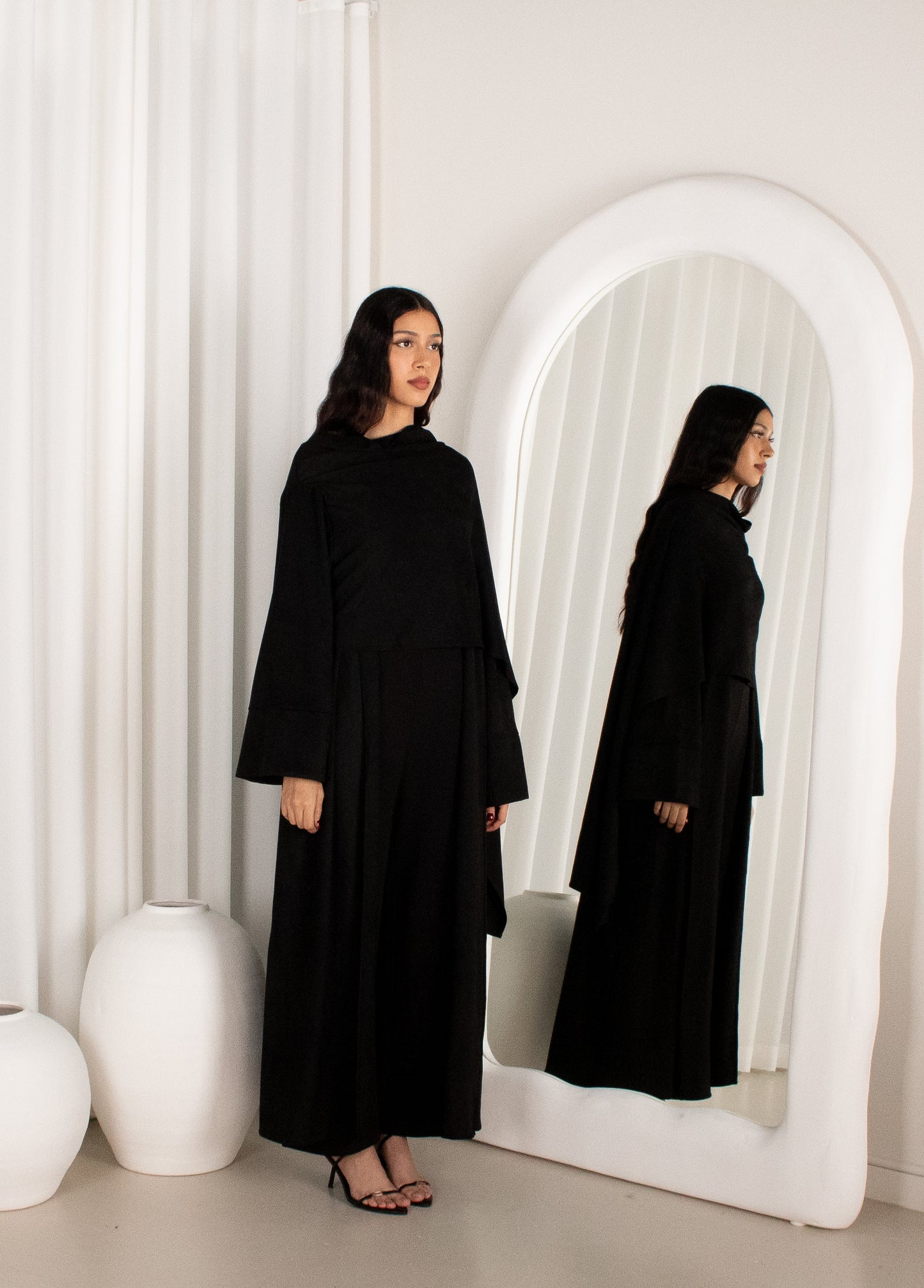 Woman in a black dress standing in front of a white mirror.