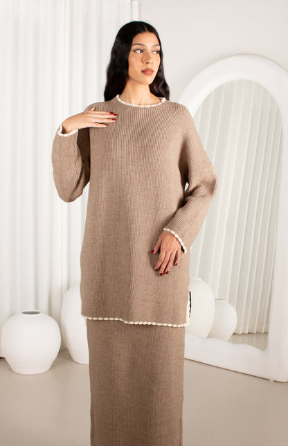 Woman wearing a beige sweater dress in a minimalistic room.