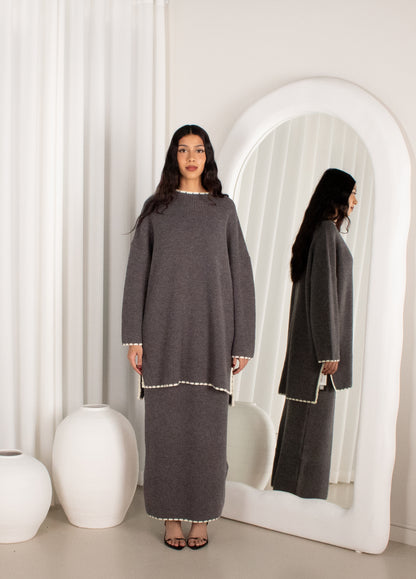 Woman wearing a gray dress standing in front of a mirror in a minimalistic room.