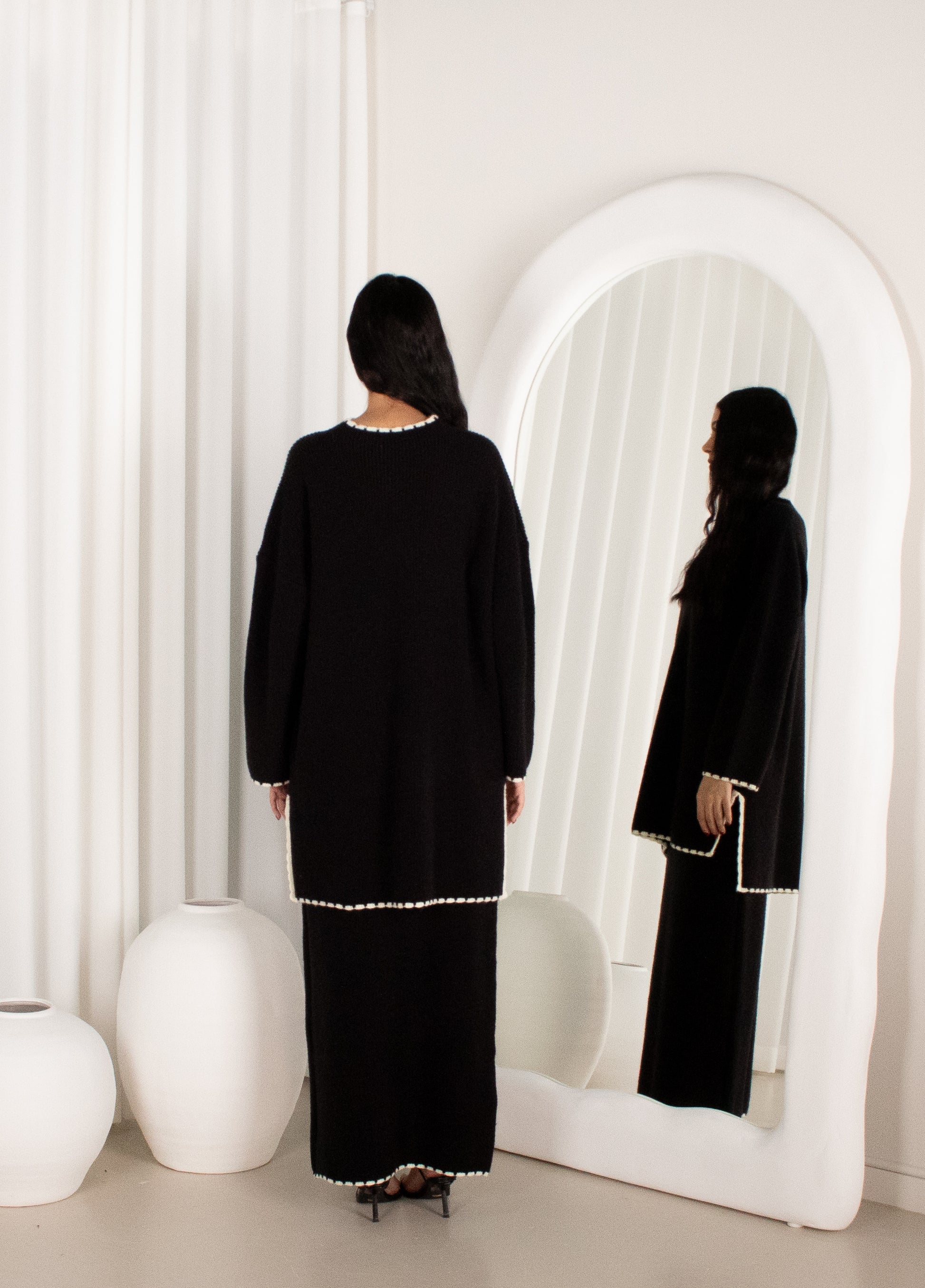 Person wearing a black outfit with white trim standing in front of a mirror.