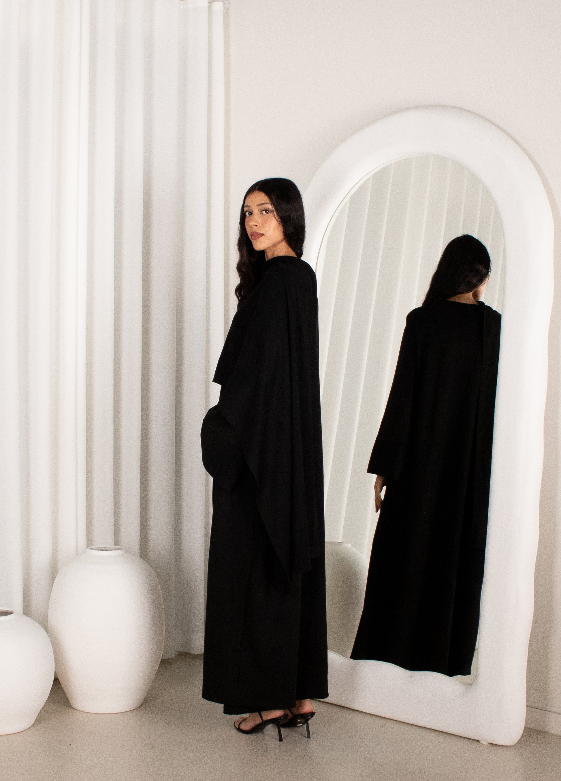 Woman in a black outfit standing in front of a white archway.