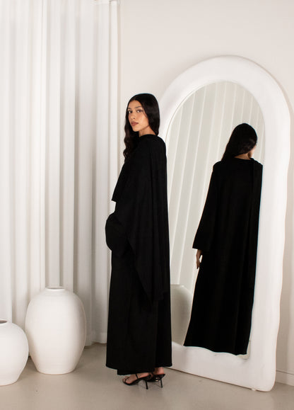 Woman in a black outfit standing in front of a white archway.