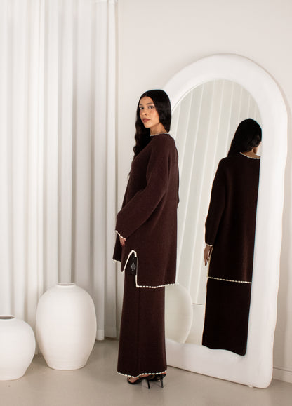 Woman in a brown dress standing in front of a white mirror with a white curtain background.