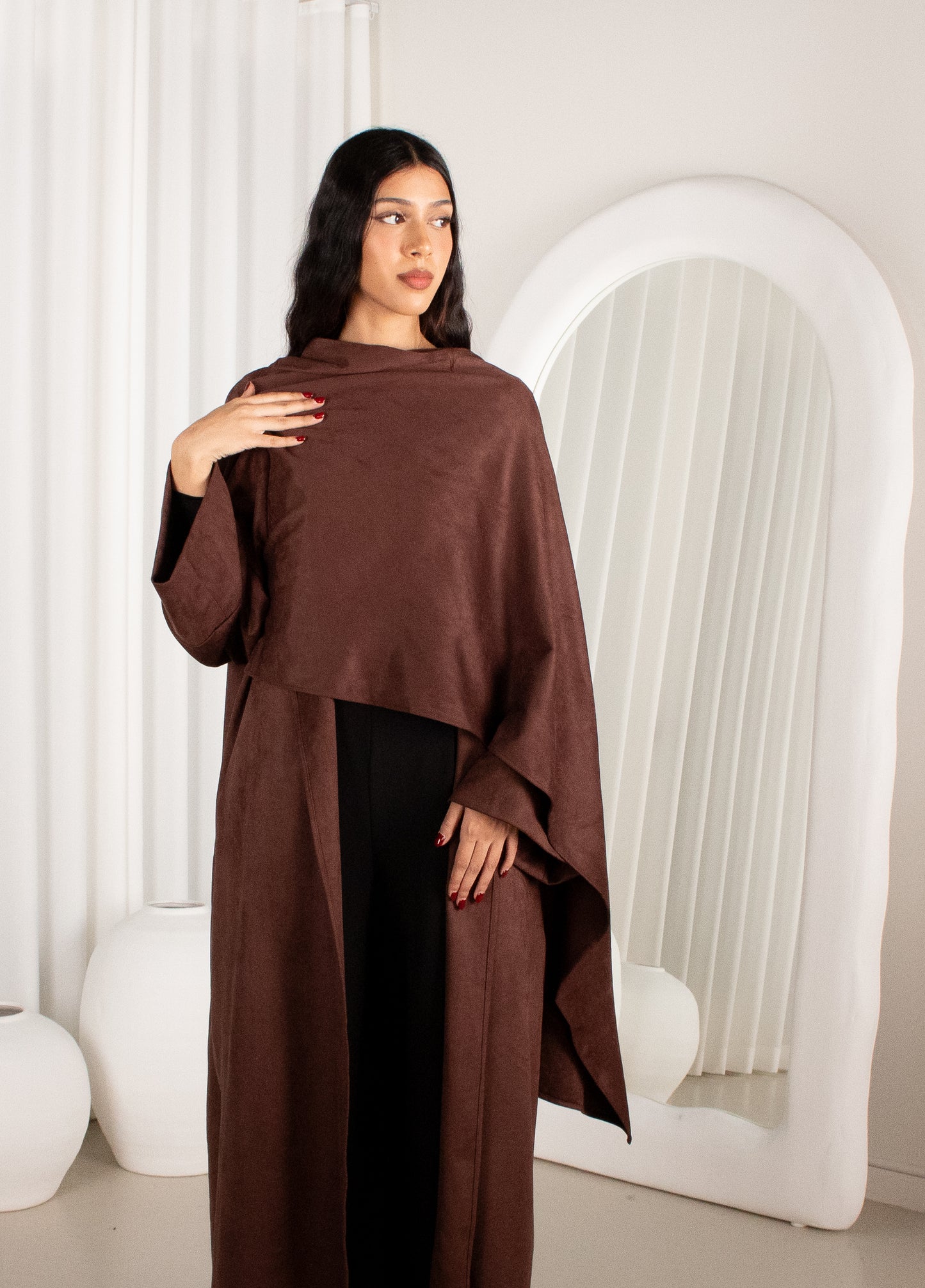 Woman wearing a brown poncho in a minimalistic setting