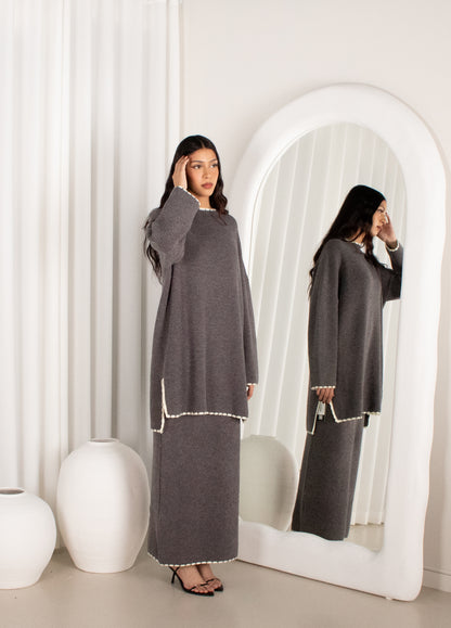 Woman in a gray dress standing in front of a mirror in a minimalistic room.