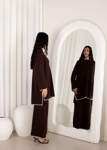 Woman in a dark brown outfit standing in front of a white mirror.
