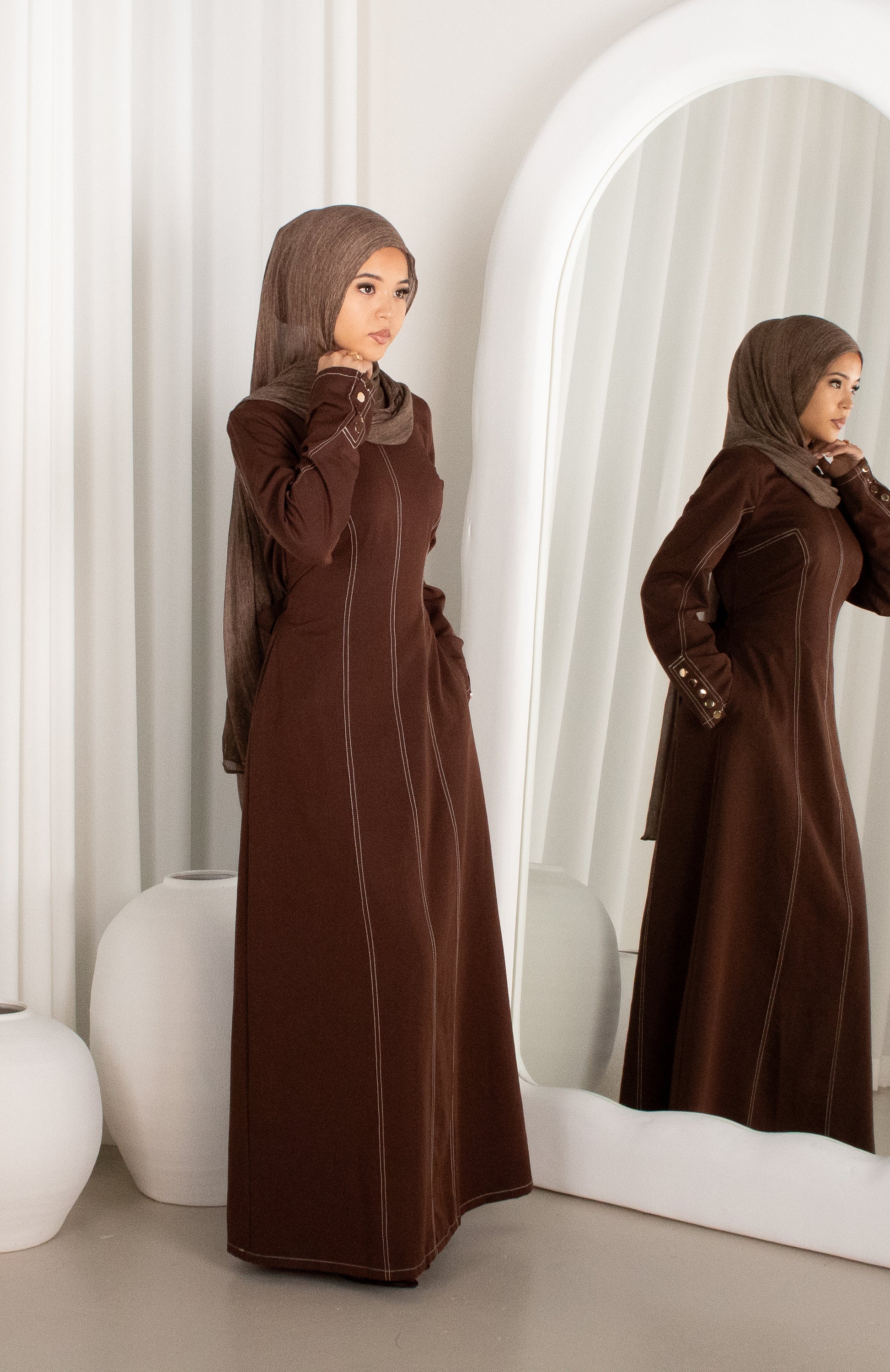 Woman in a brown abaya standing in front of a mirror.