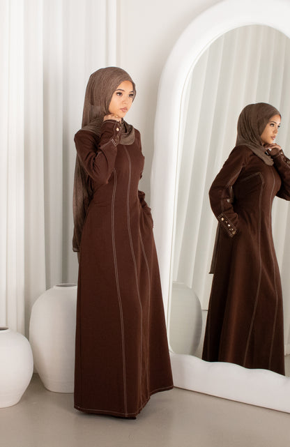 Woman in a brown abaya standing in front of a mirror.