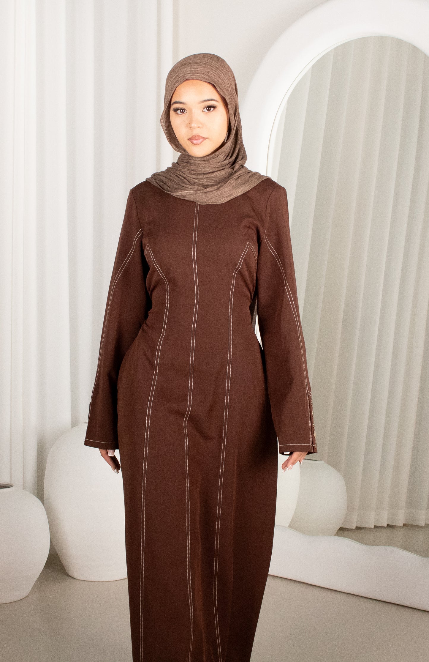 Woman wearing a brown abaya and hijab in a modern interior setting