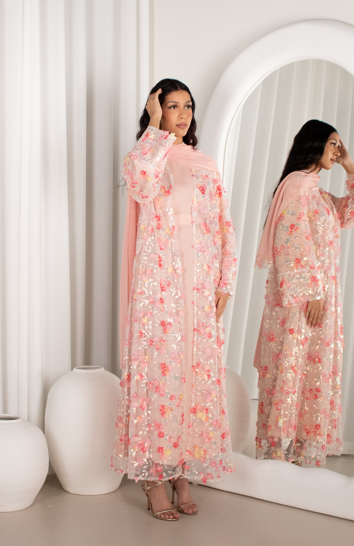 Woman in a floral dress standing in front of a mirror in a minimalistic room.