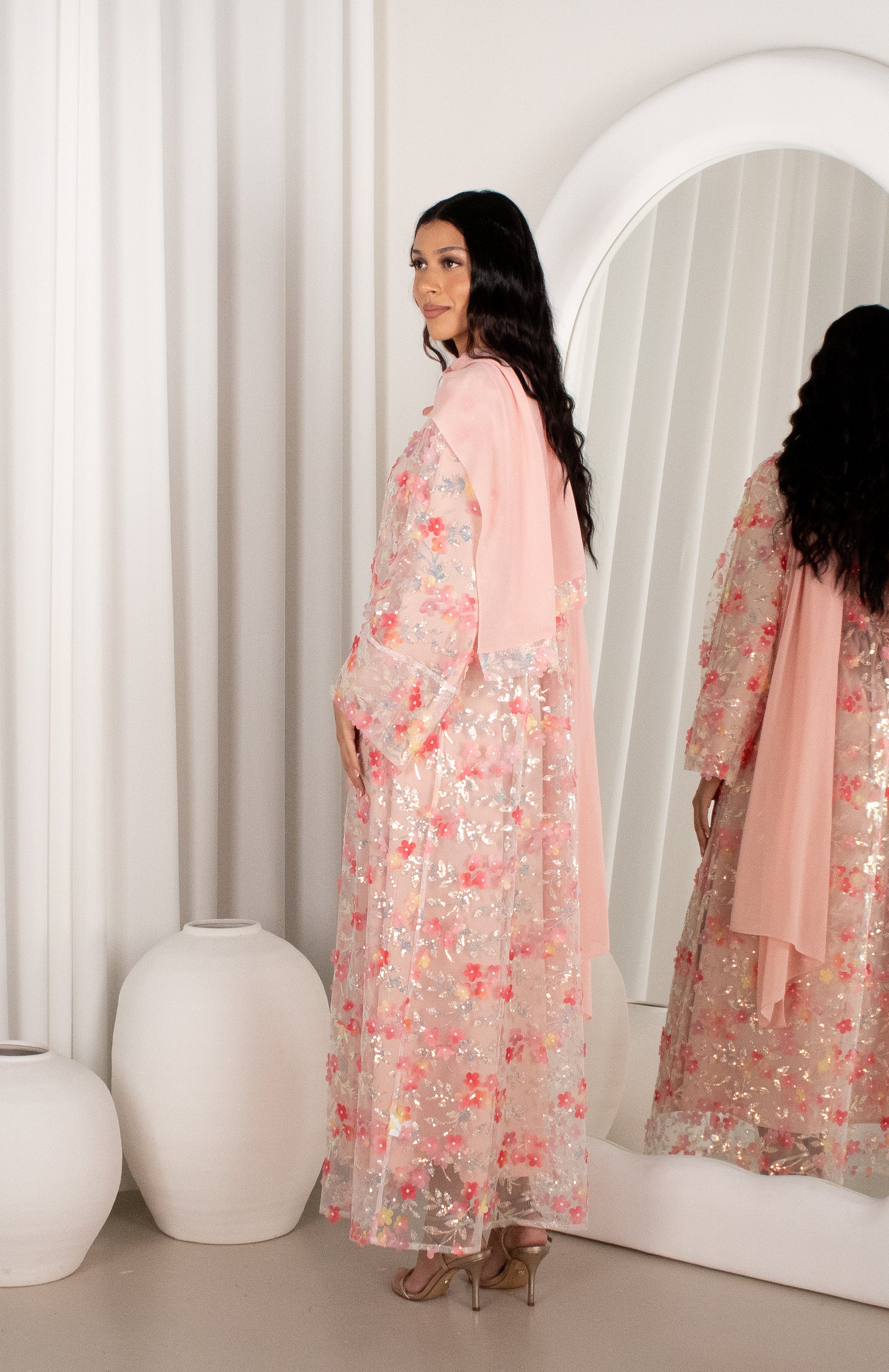 Woman in a floral dress standing in front of a mirror in a minimalistic room.