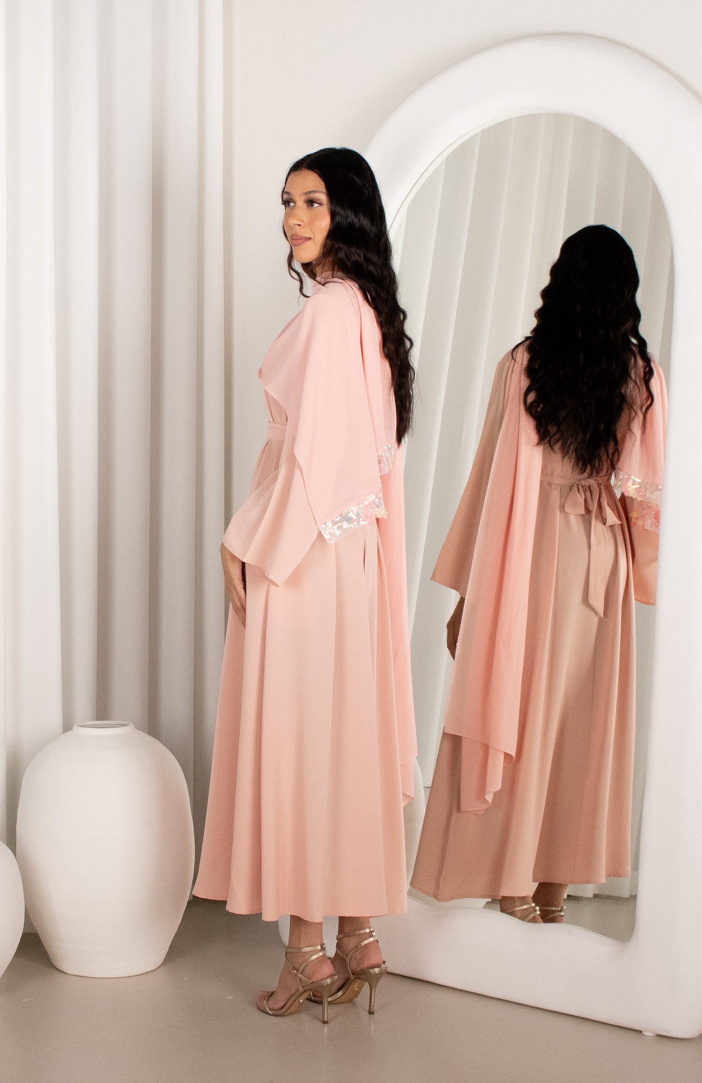 Woman in a pink outfit standing in front of a mirror with a white curtain background