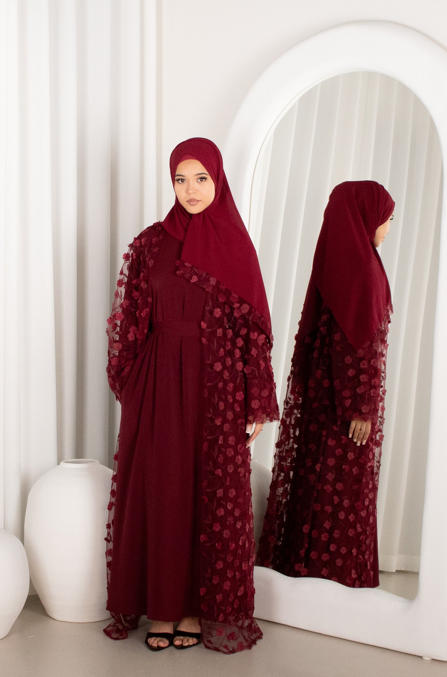 Woman wearing a burgundy abaya with floral details in front of a mirror.