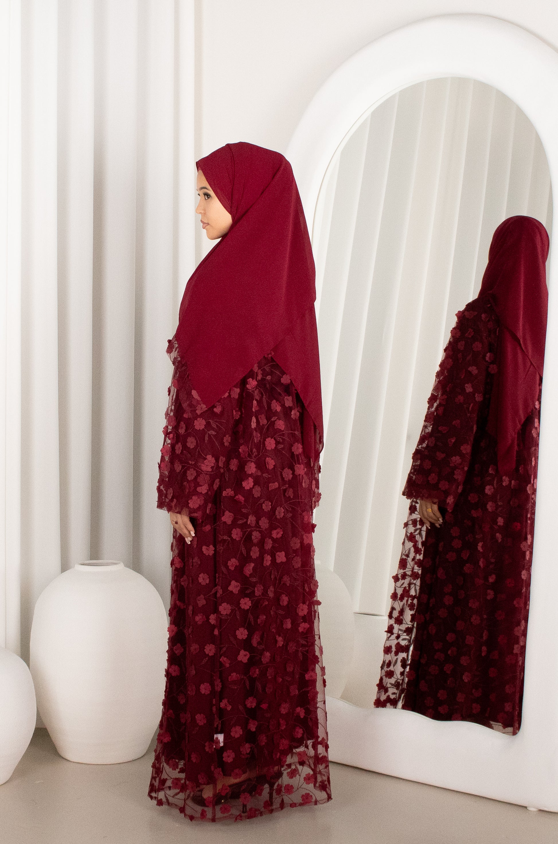 Woman wearing a burgundy dress with floral patterns standing in front of a mirror.