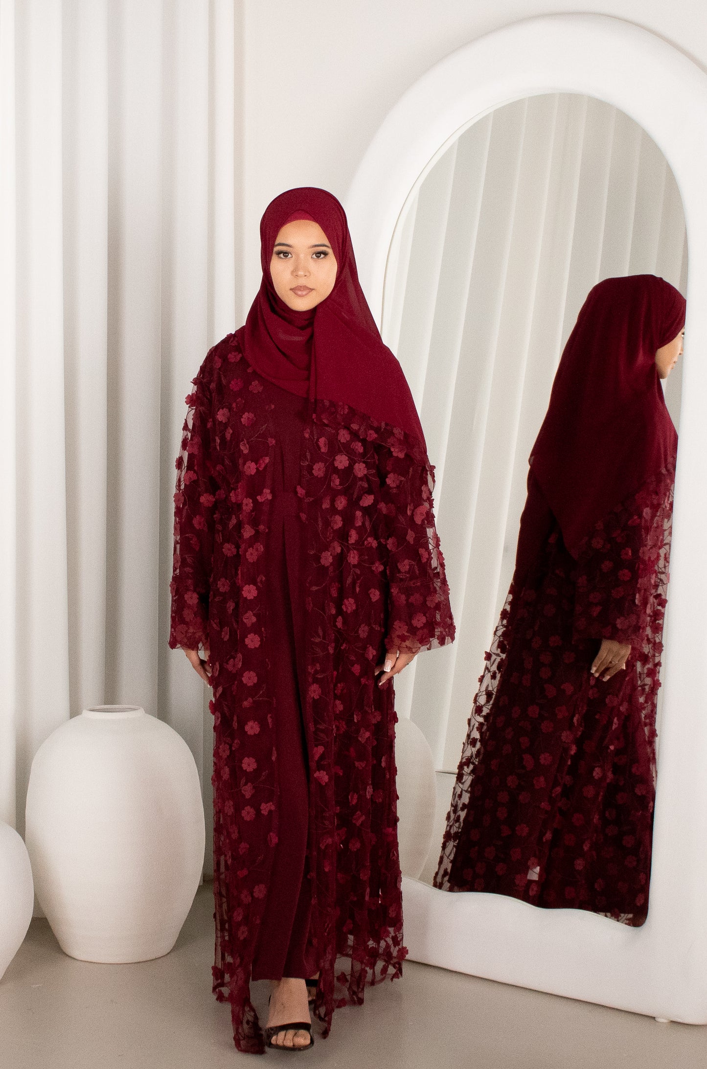 Woman in a burgundy floral abaya standing in front of a mirror.