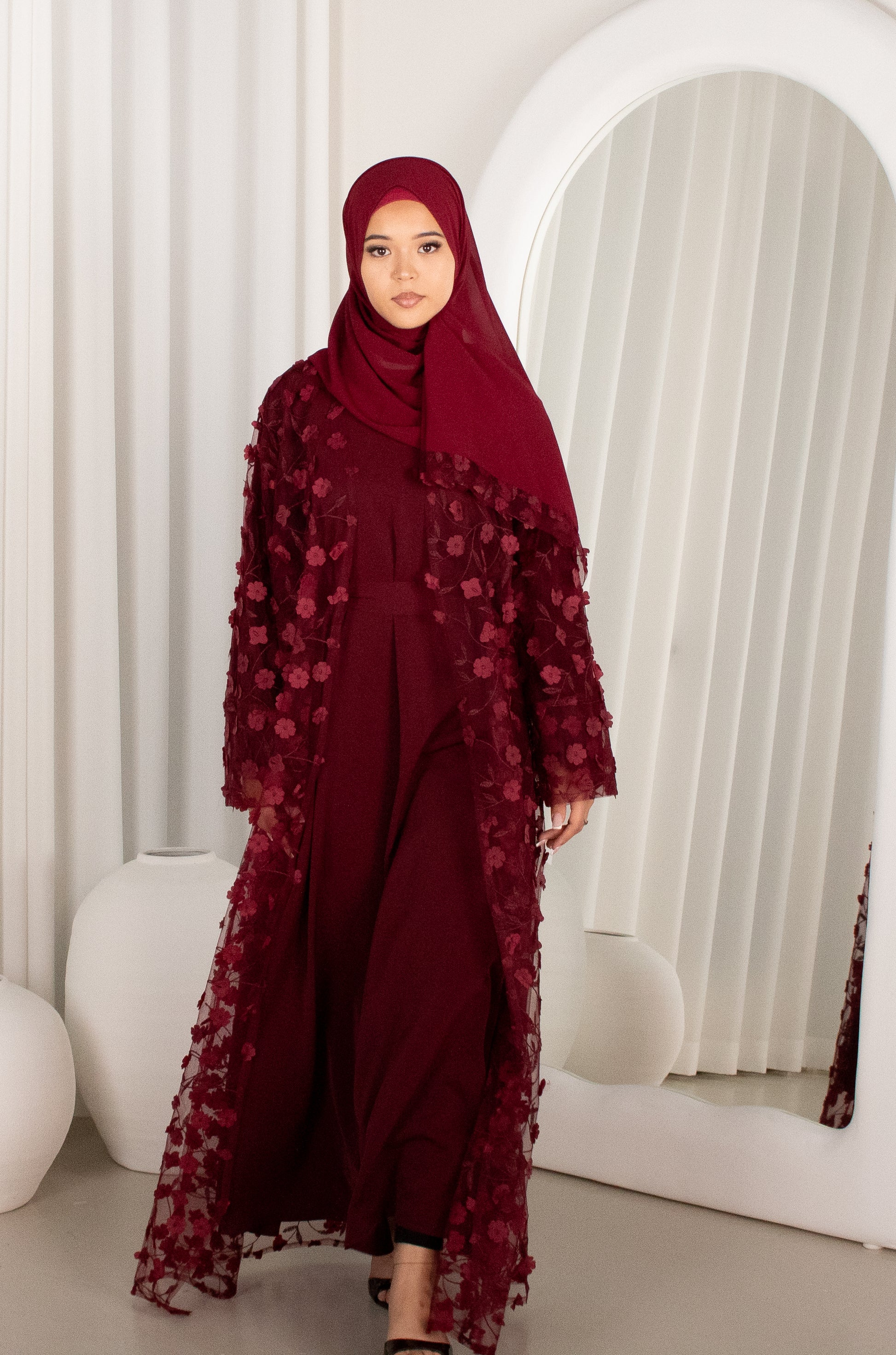 Woman wearing a burgundy outfit with a matching hijab in a minimalistic setting.