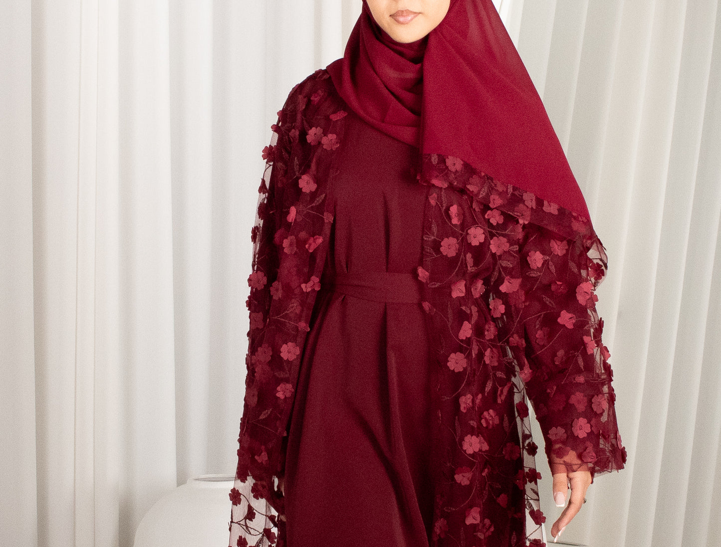 Maroon dress with floral lace overlay and matching hijab against a white curtain background