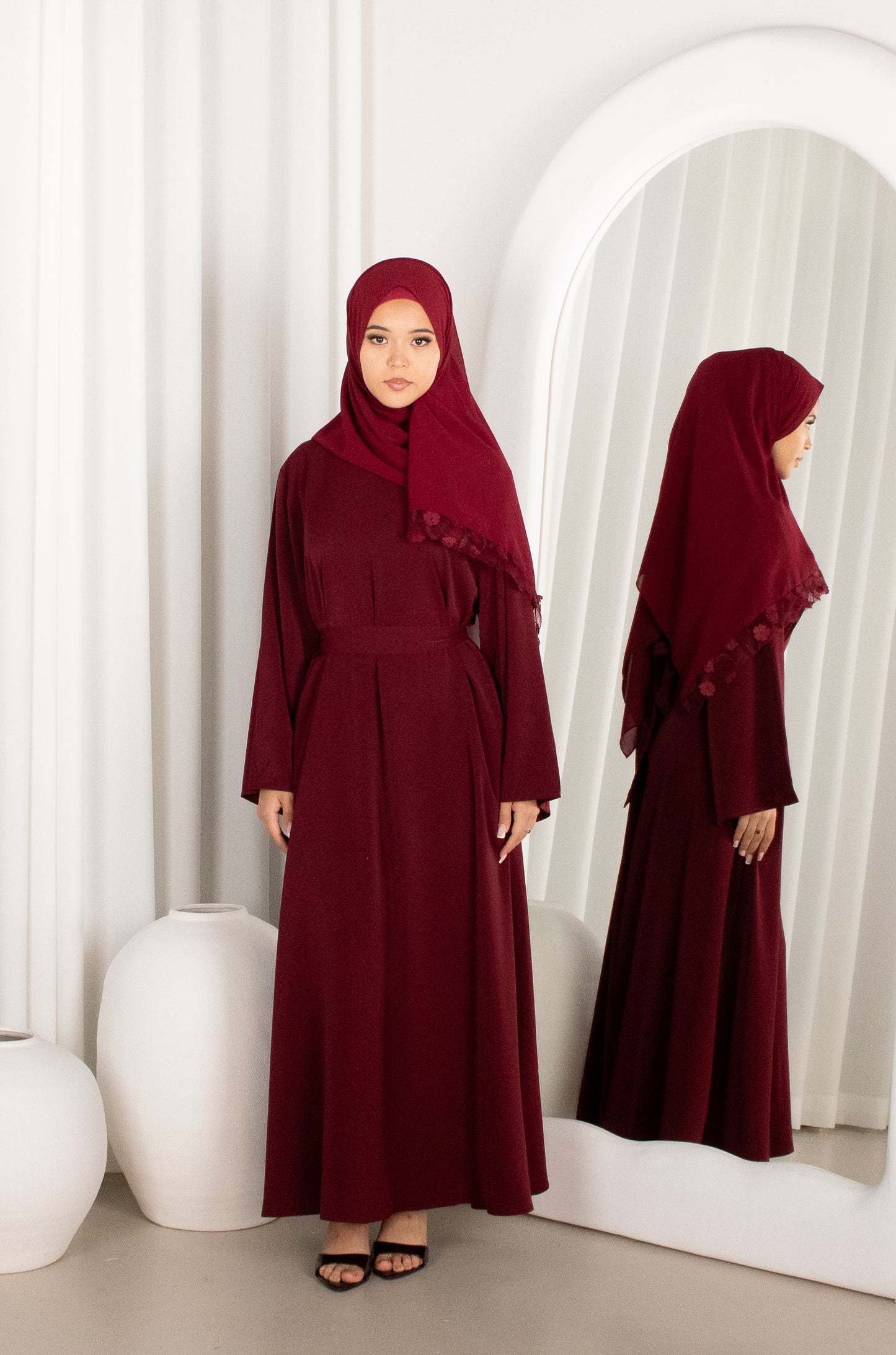 Woman in a burgundy dress and hijab standing in front of a mirror.