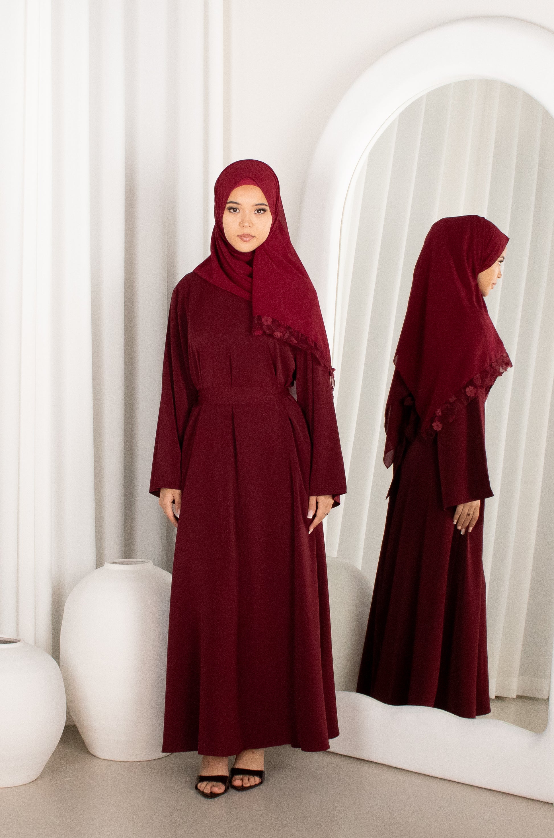 Woman in a burgundy dress and hijab standing in front of a mirror.