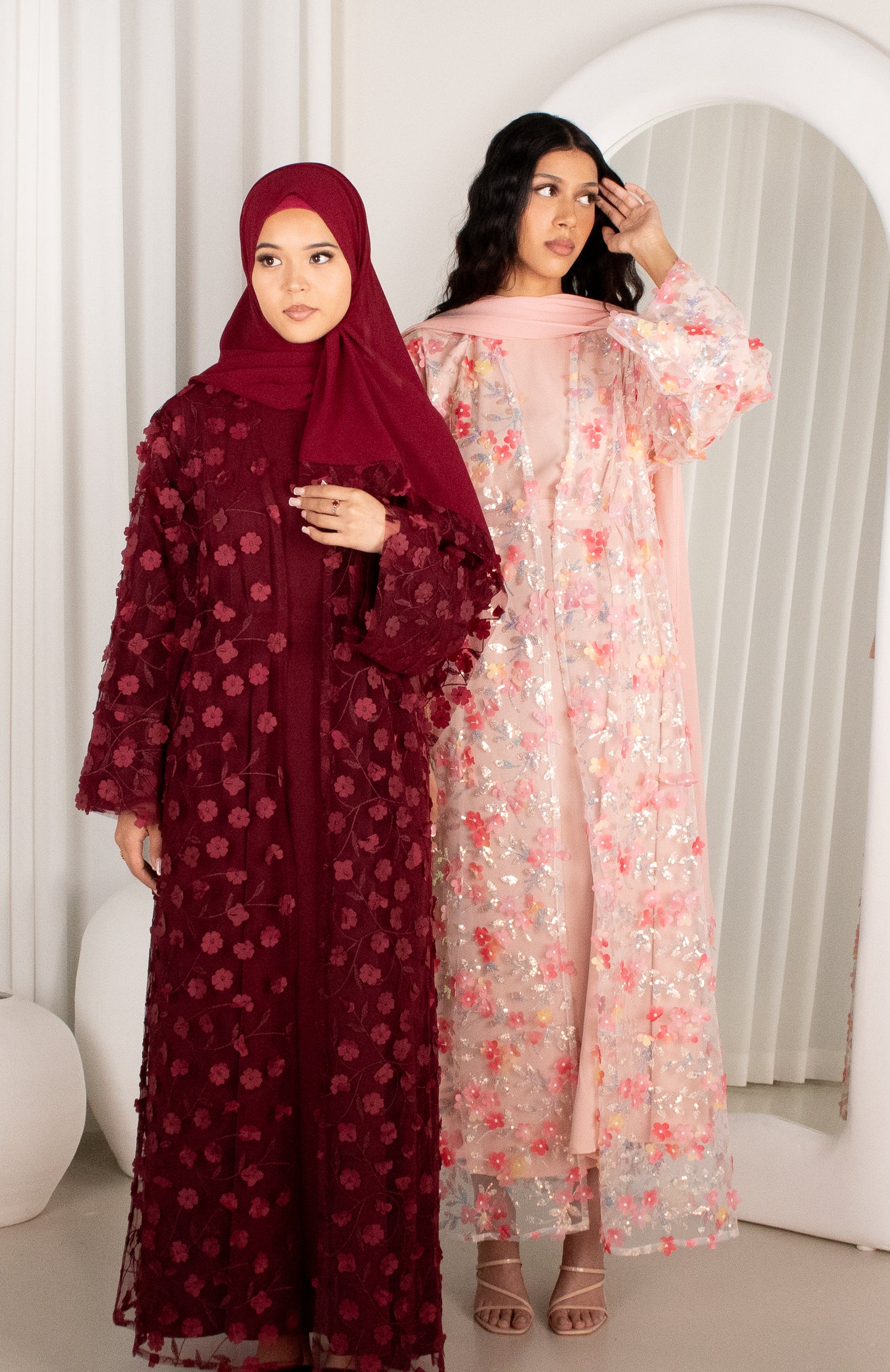 Two women wearing floral dresses standing in a modern interior setting.