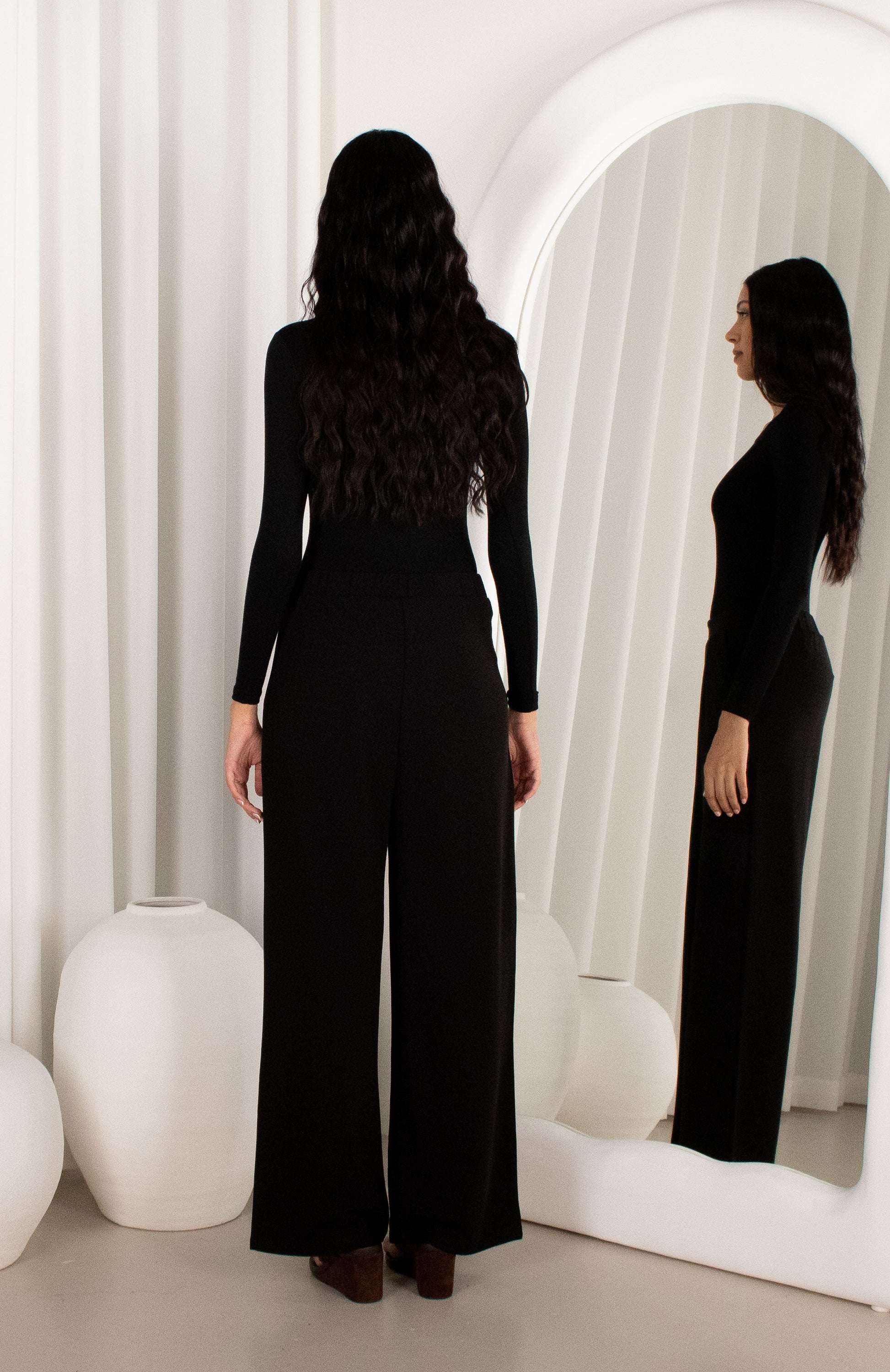 Woman wearing a black jumpsuit standing in front of a mirror.