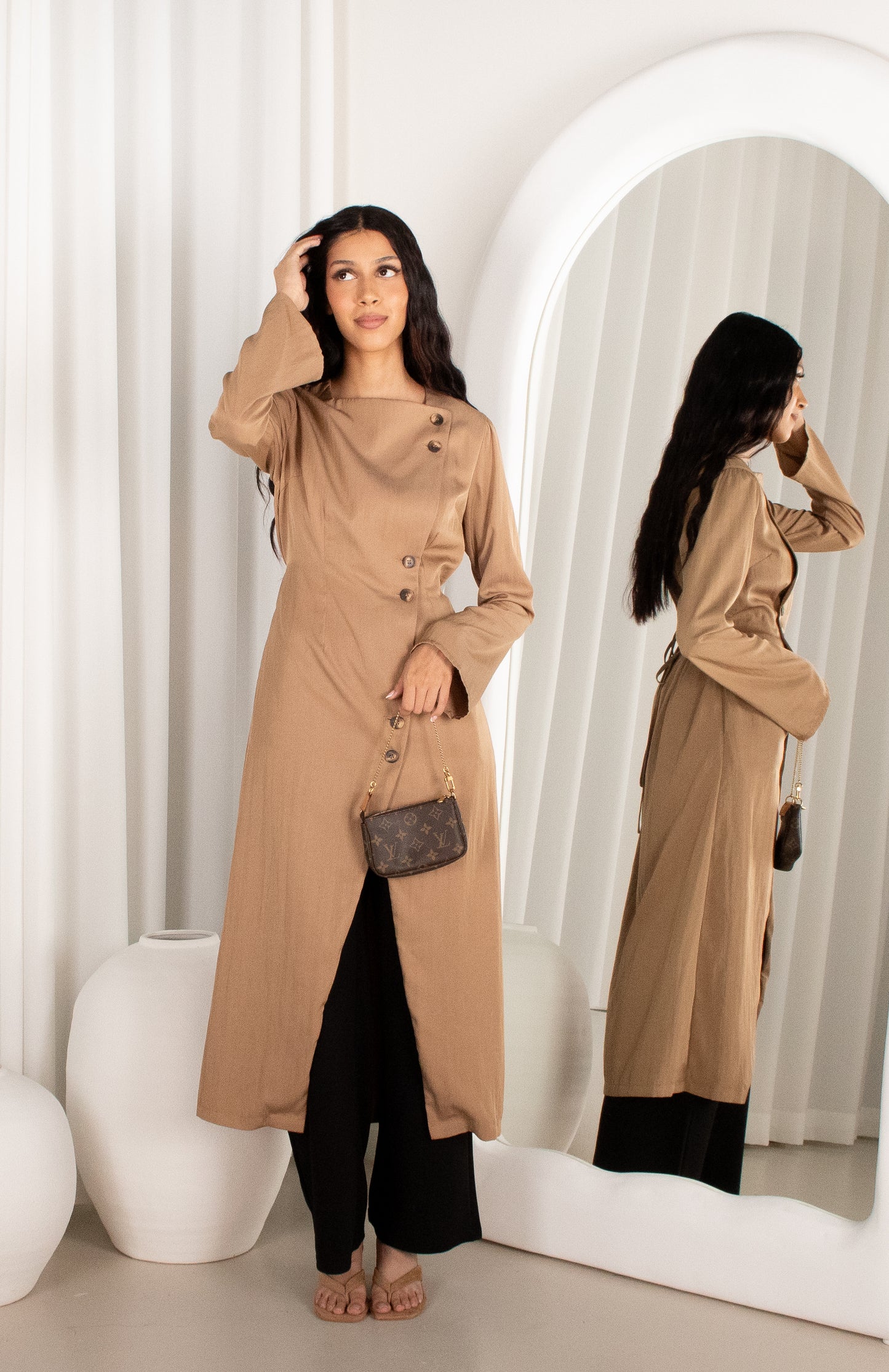 Woman wearing a beige trench coat in front of a mirror.