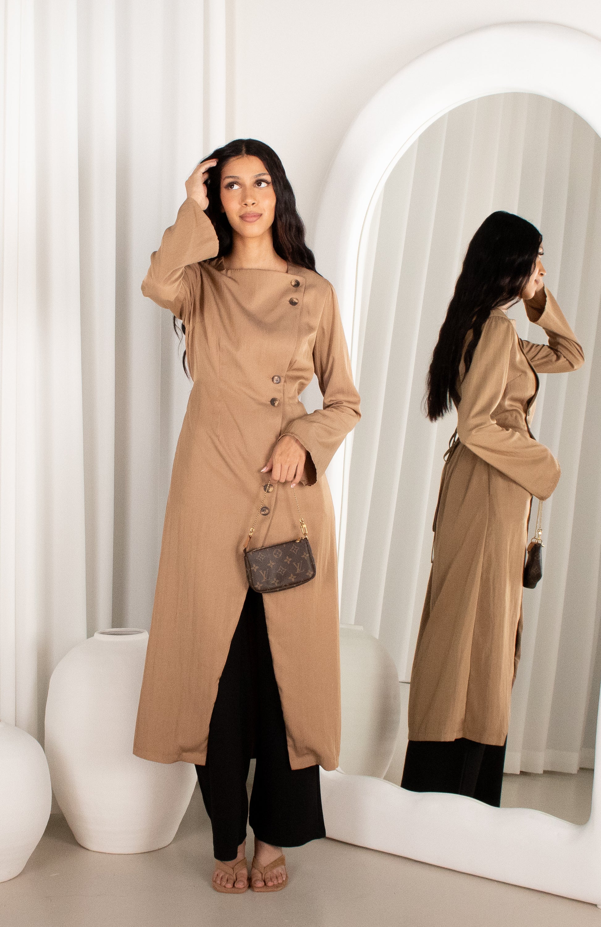 Woman wearing a beige trench coat in front of a mirror.