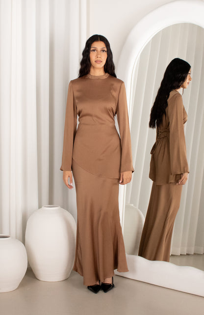 Woman wearing a brown outfit standing in front of a mirror with a white curtain background.