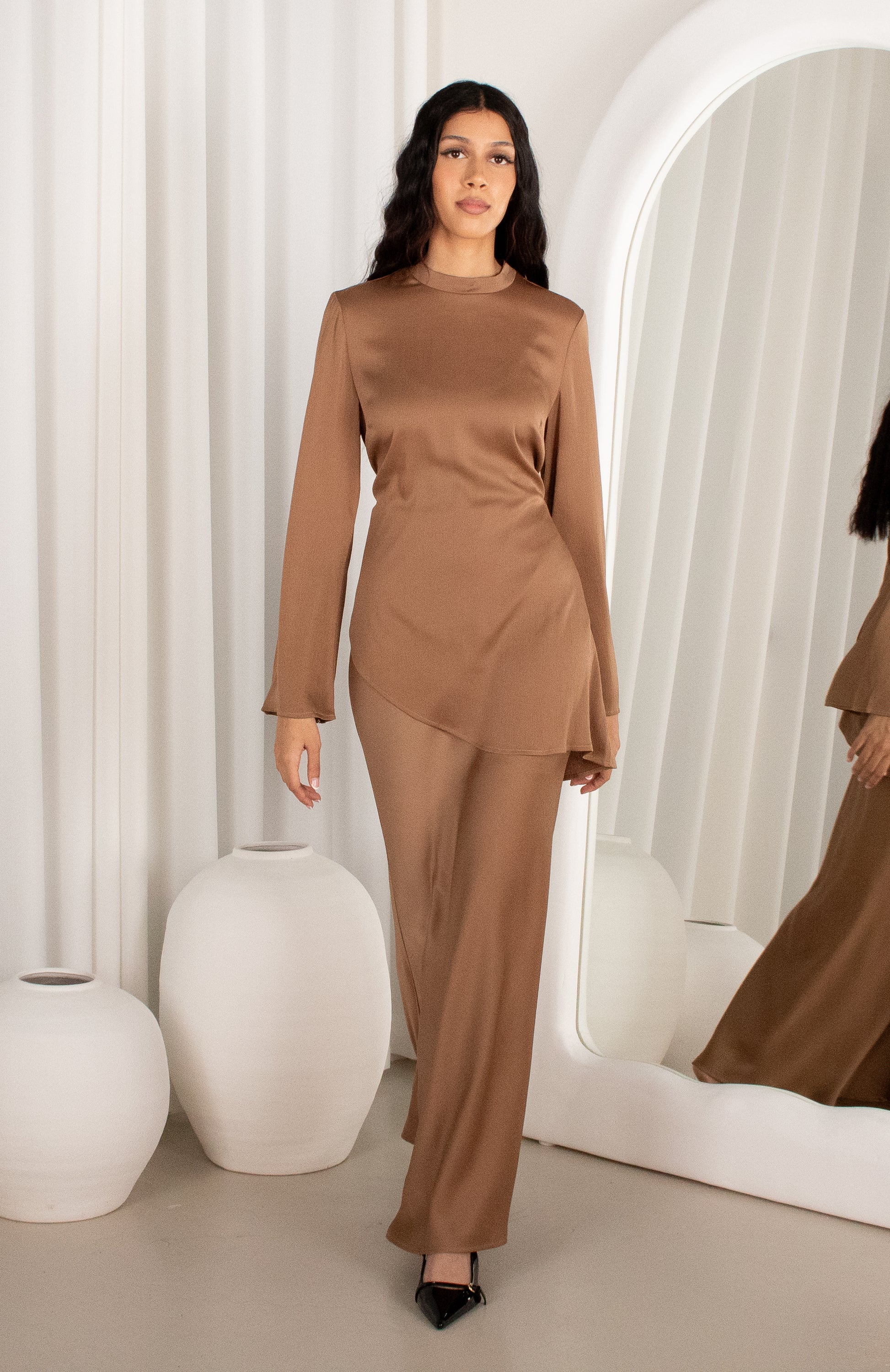 Woman wearing a brown outfit standing in a modern interior setting with white walls and decor.