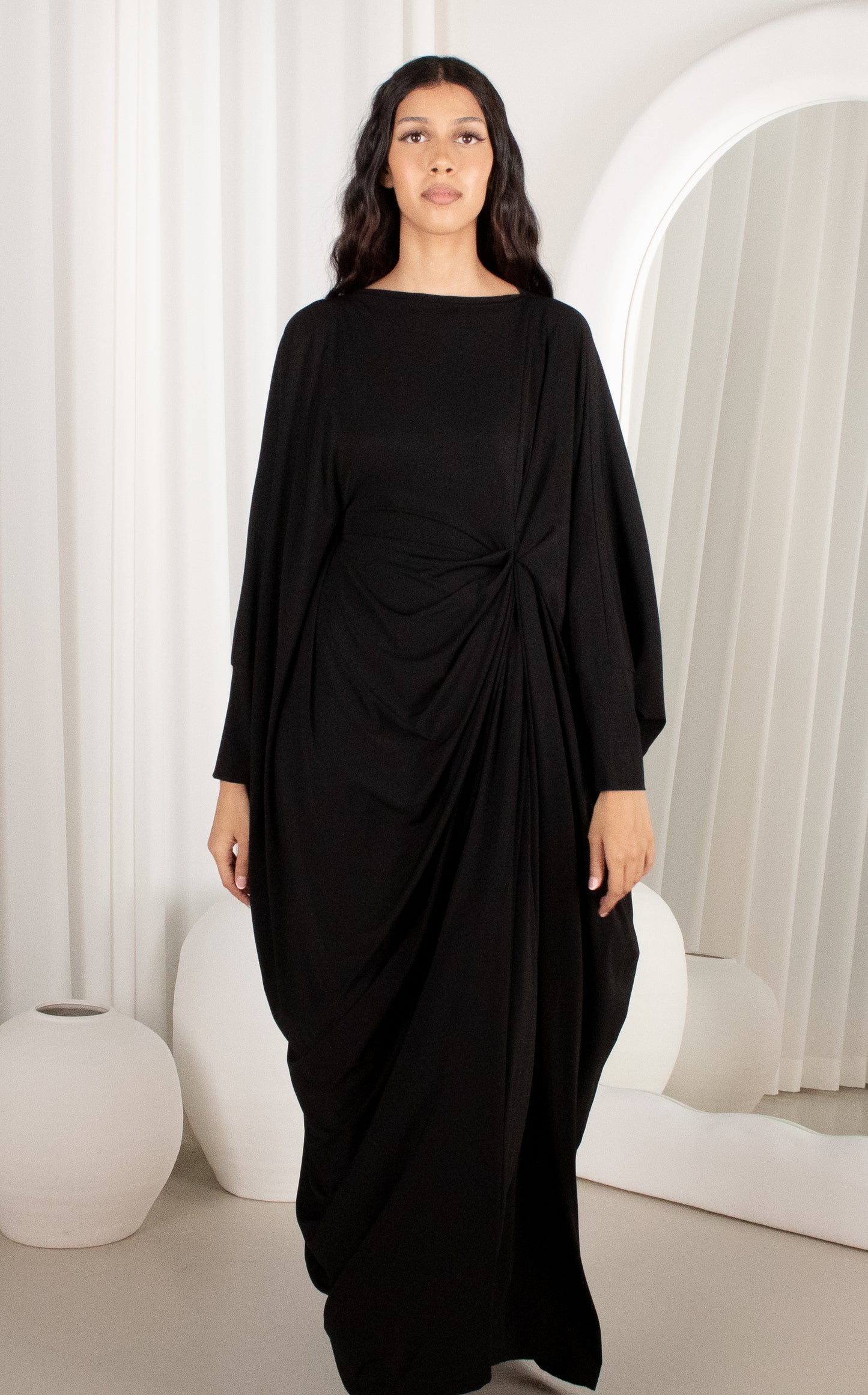 Woman wearing a black draped dress in a minimalistic setting