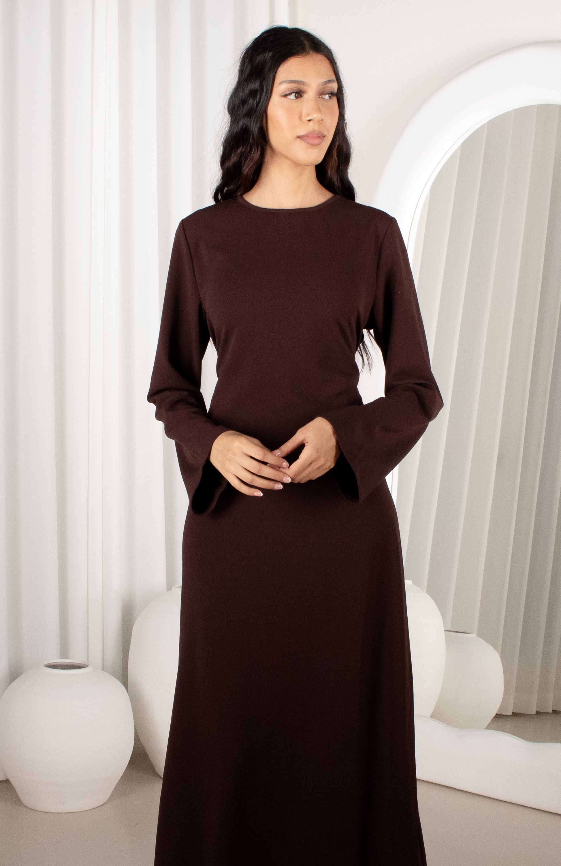 Woman wearing a brown dress in a minimalistic room with white curtains and decor.