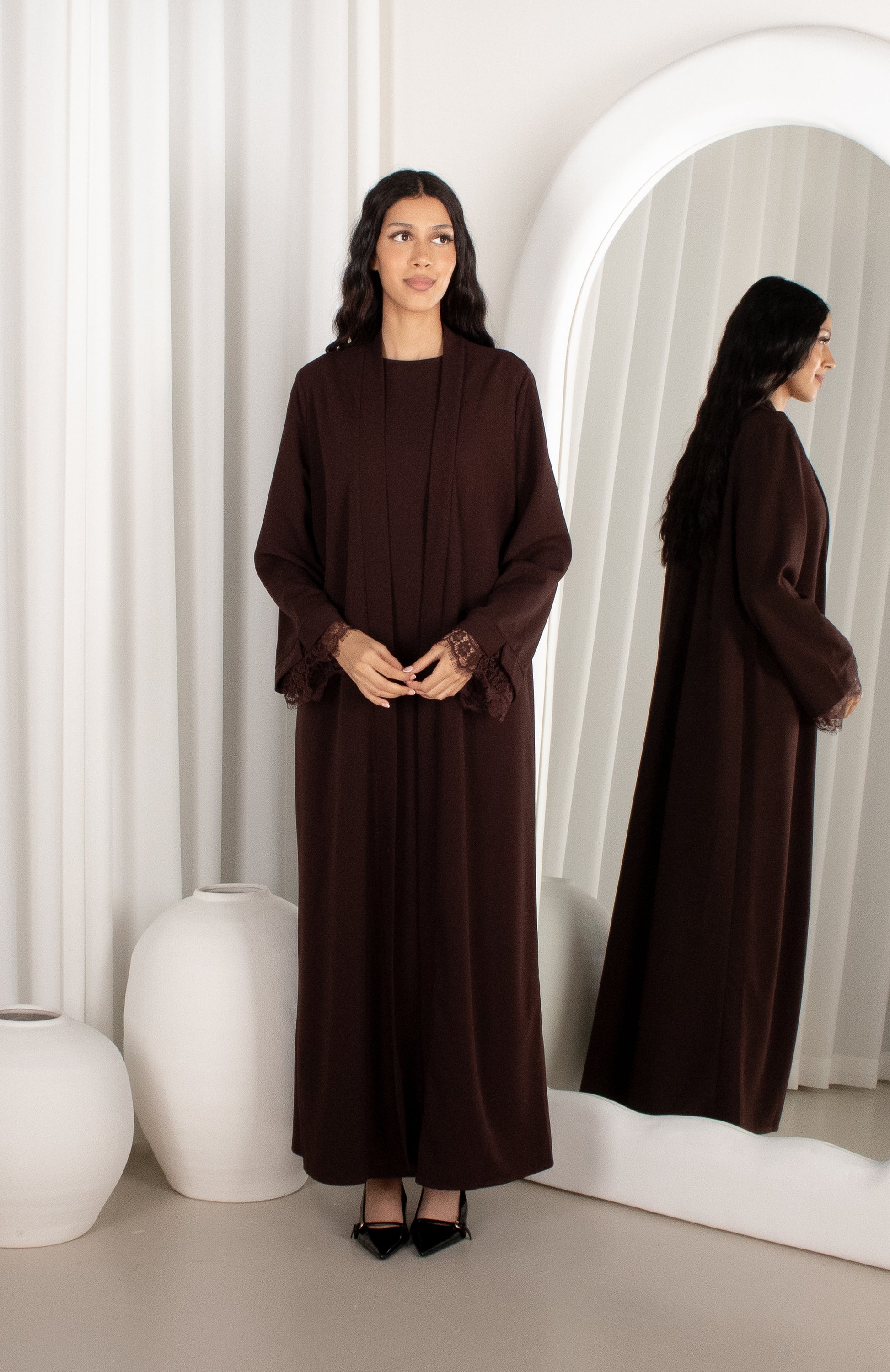 Woman wearing a brown long dress standing in front of a mirror.