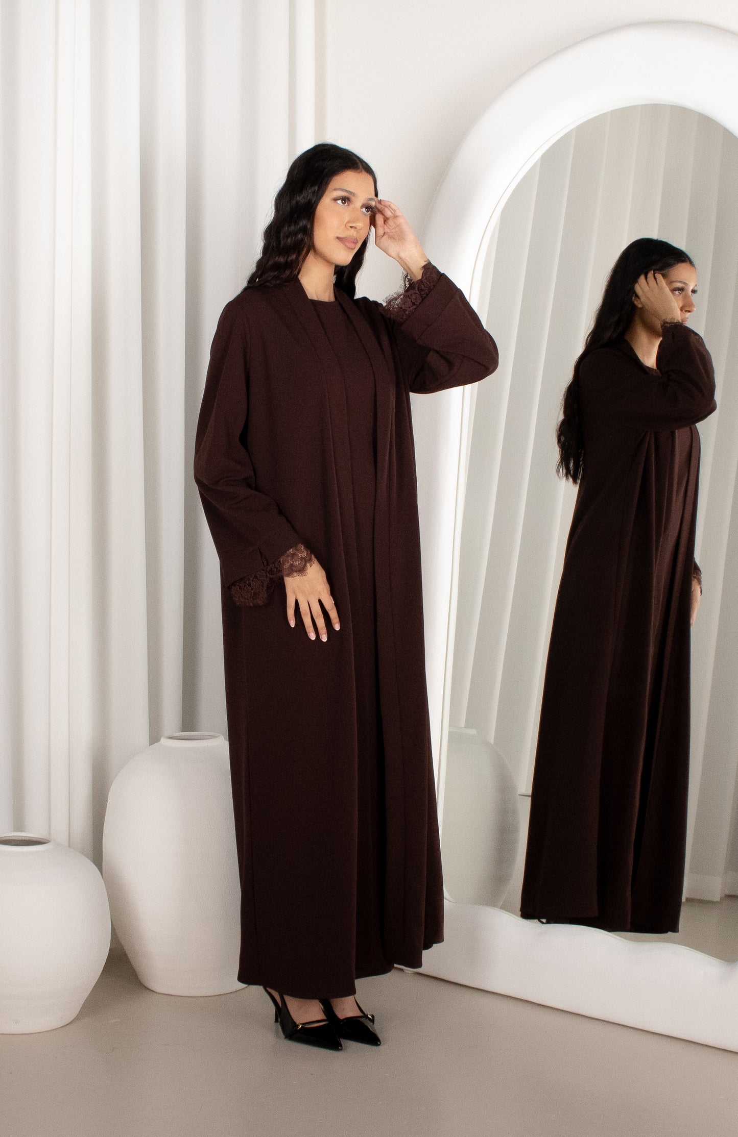 Woman in a brown dress standing in front of a mirror in a minimalistic room.