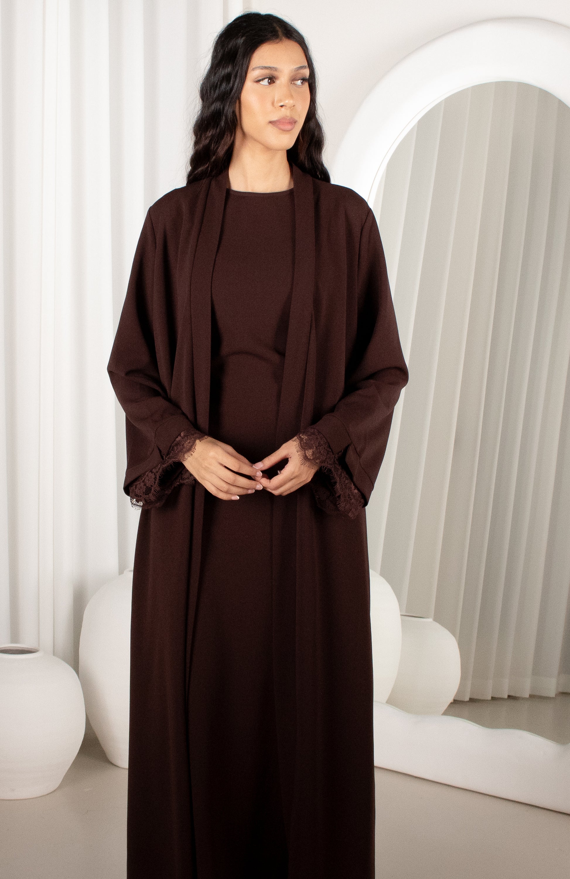 Woman wearing a brown dress with a matching shawl in a minimalistic setting.