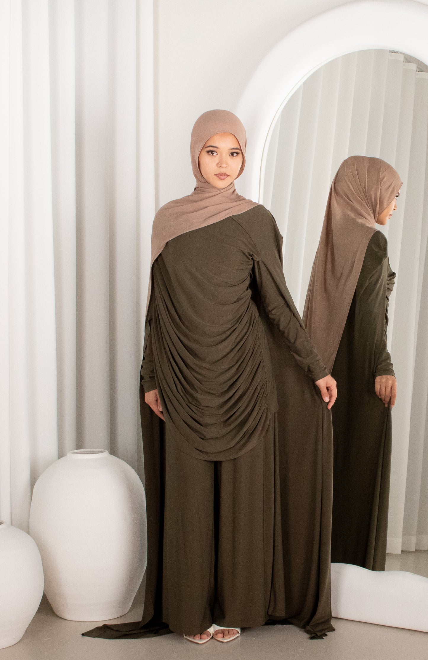Woman wearing a brown dress and hijab standing in front of a mirror.