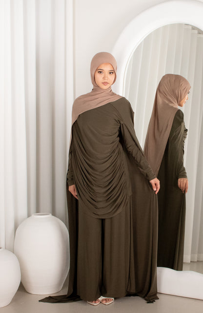 Woman wearing a brown dress and hijab standing in front of a mirror.