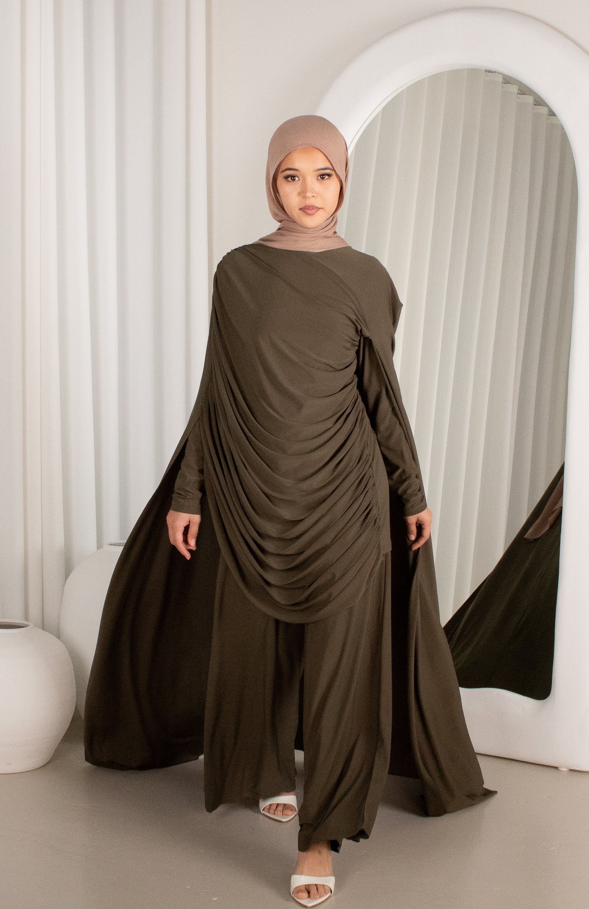 Woman wearing a long, flowing olive green dress standing in front of a mirror.