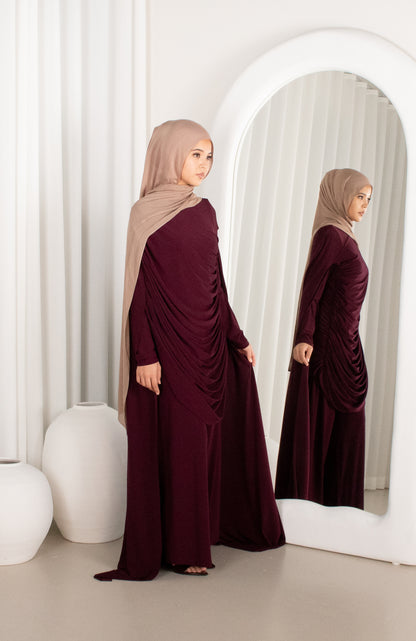Woman in a burgundy dress and beige hijab standing in front of a mirror.