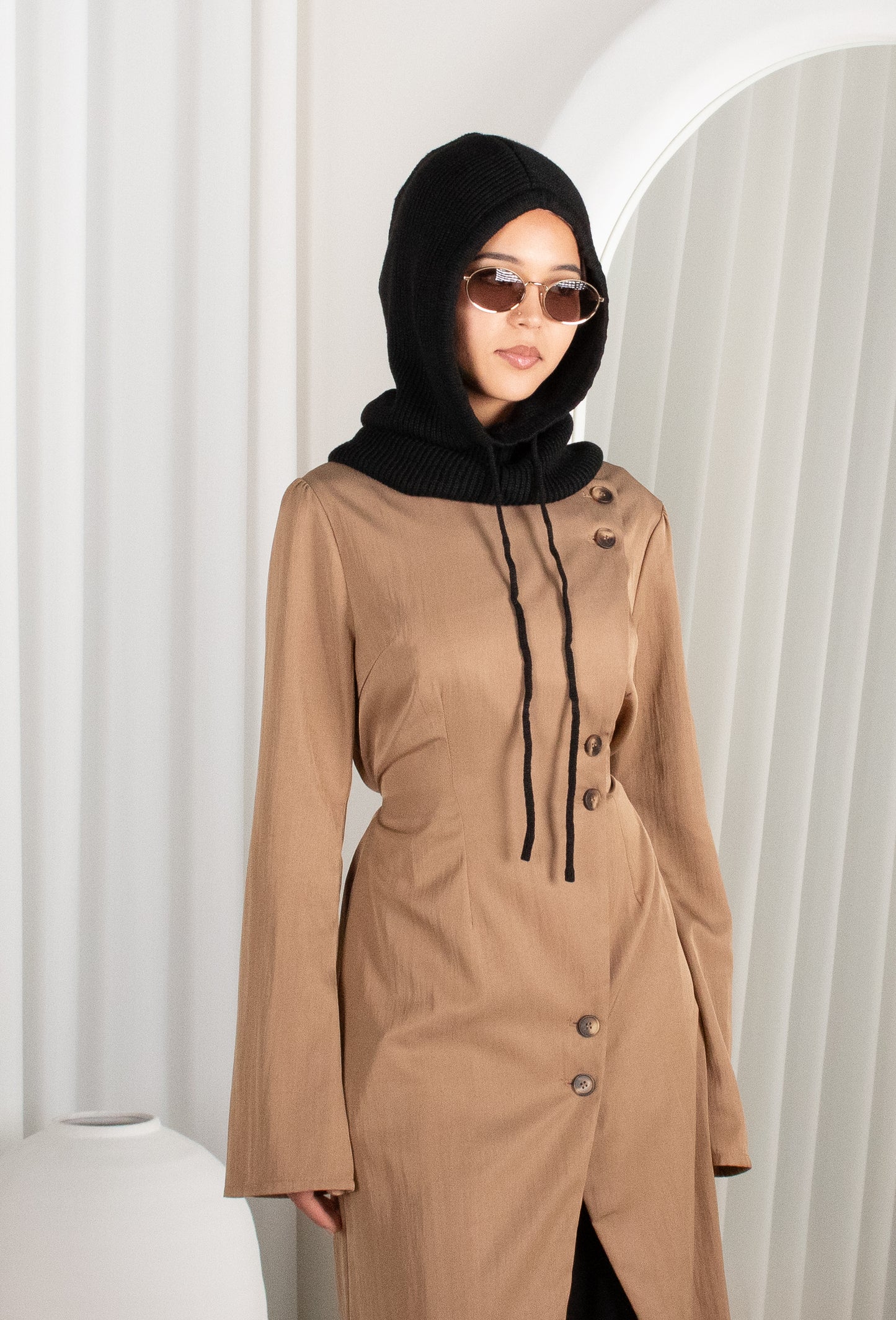 Woman wearing a brown dress with a black hijab against a white background