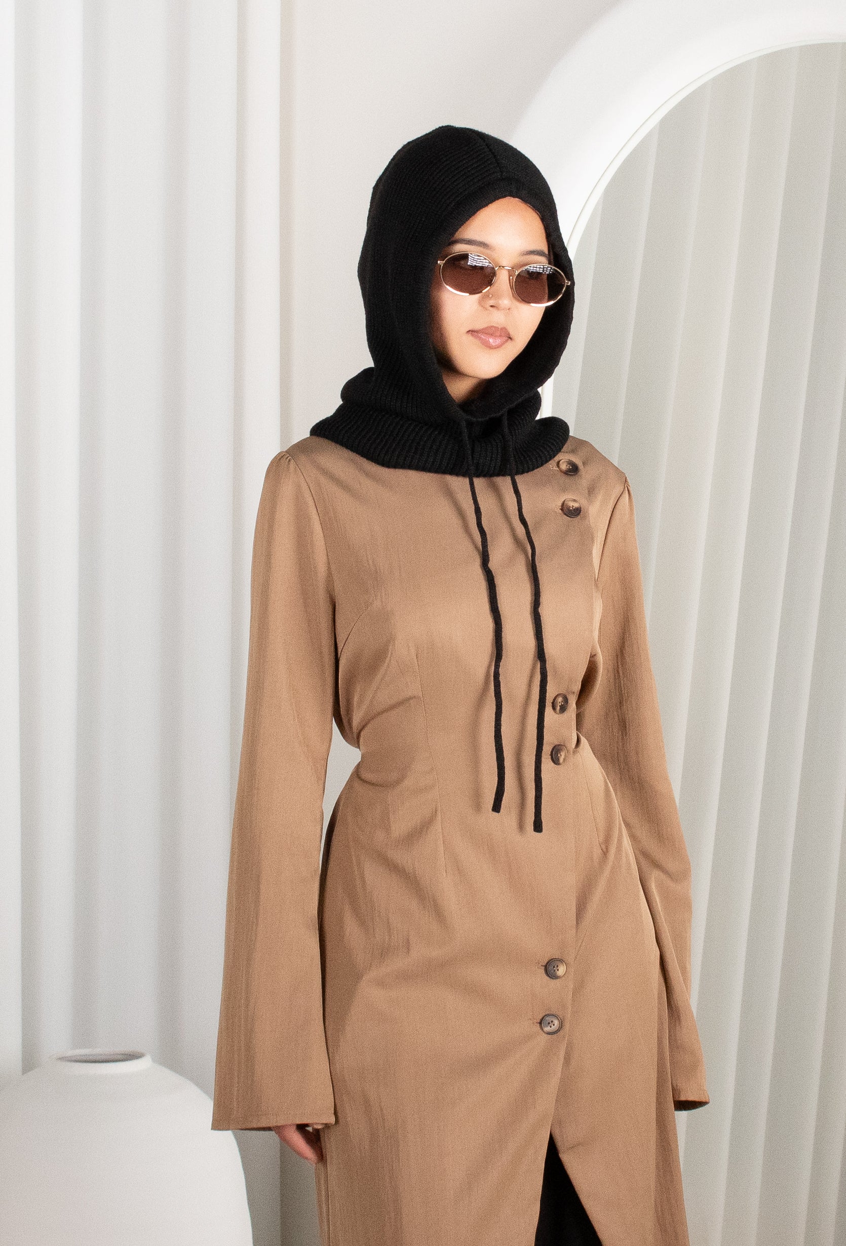 Woman wearing a brown dress with a black hijab against a white background