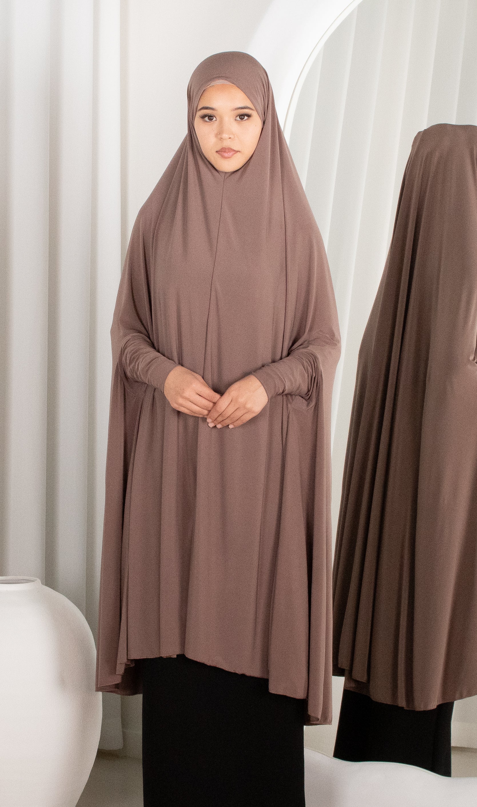 Woman wearing a brown abaya in front of a white curtain
