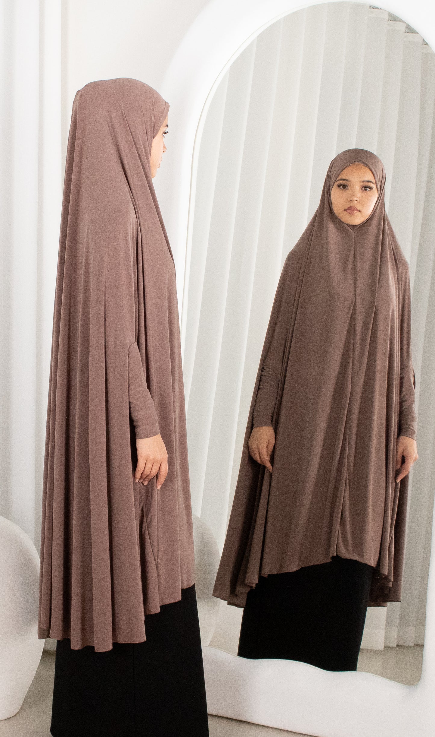 Woman wearing a brown abaya in front of a mirror.
