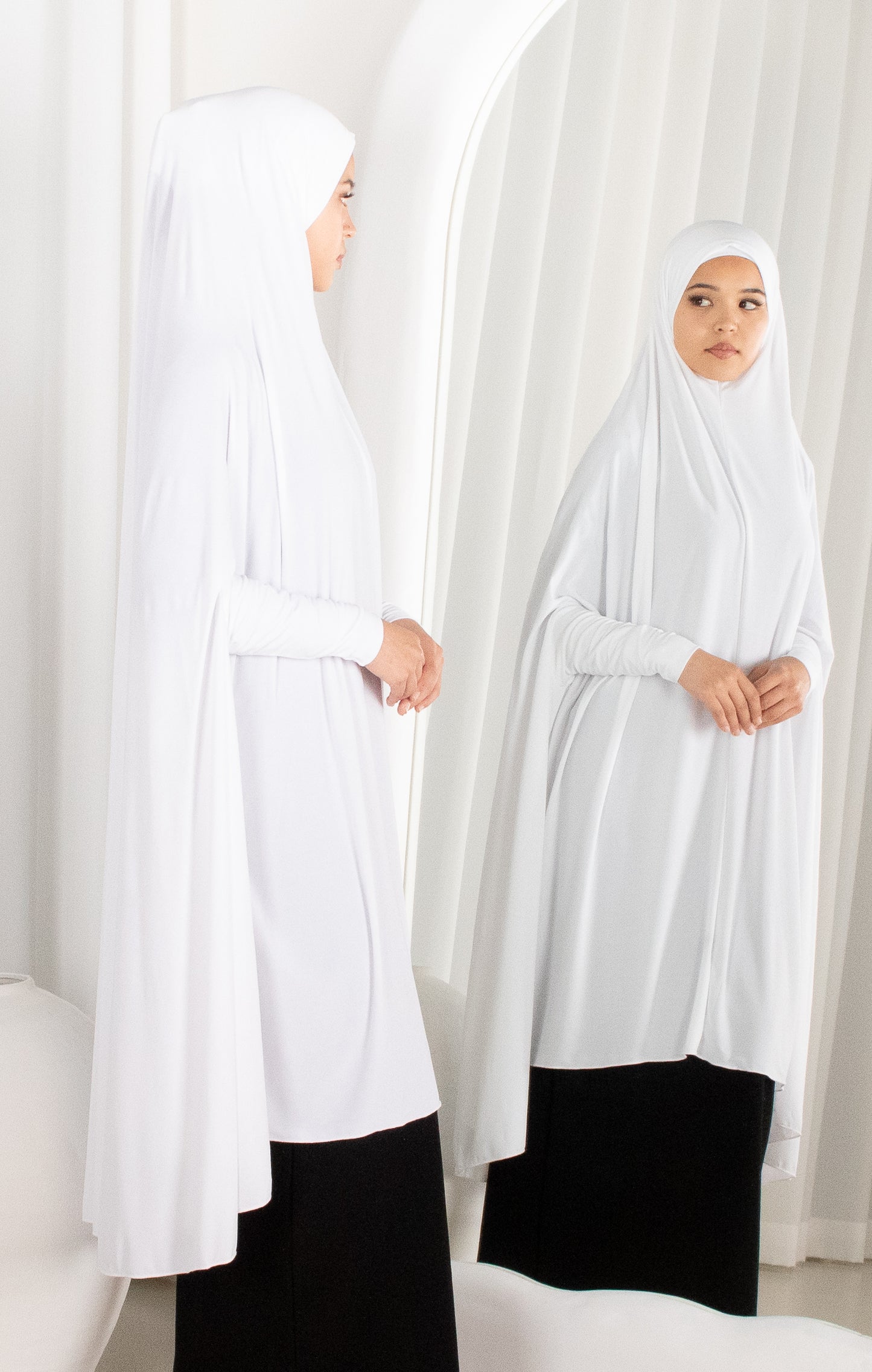 Two women wearing white hijabs and black下半身服饰 in a minimalistic setting.